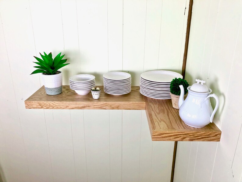 Puede incluir: Una estanter&iacute;a de esquina de madera con una tetera blanca, una suculenta en maceta y pilas de platos blancos.