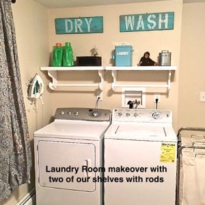 Puede incluir: Un cuarto de lavado blanco con dos estantes blancos con barras, una secadora blanca y una lavadora blanca. Los estantes tienen una variedad de art&iacute;culos, incluyendo dos botellas verdes, una caja negra, un contenedor azul con la etiqueta "Laundry" y una peque&ntilde;a figura de mono. Las paredes est&aacute;n pintadas de un color beige claro. Las palabras "DRY" y "WASH" est&aacute;n escritas en dos letreros azules sobre los estantes.