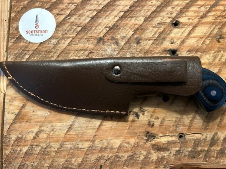 May include: A brown leather sheath with a stitched edge and a silver rivet. The sheath is holding a blue and black handled knife with a wood grain pattern.