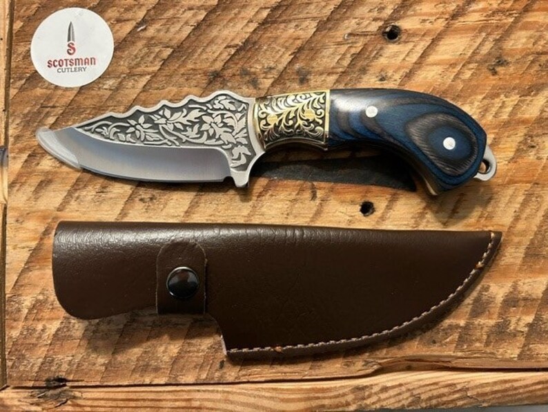 May include: A small, silver knife with a decorative floral pattern on the blade. The handle is made of dark wood with blue accents and gold accents. The knife comes with a brown leather sheath.