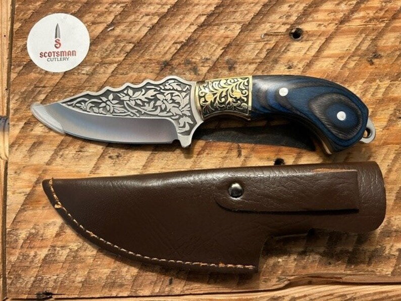 May include: A small, silver knife with a blue and black wooden handle. The knife has a floral design etched into the blade and a leather sheath.