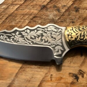 May include: A silver pocket knife with a black handle and intricate floral designs. The handle is decorated with gold accents.