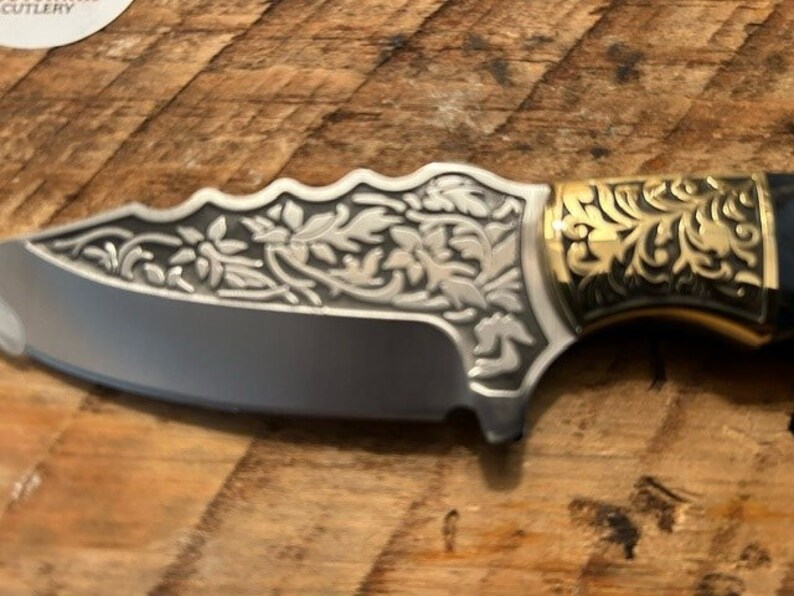 May include: A silver pocket knife with a black handle and intricate floral designs. The handle is decorated with gold accents.