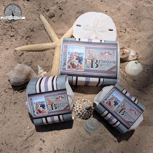 May include: Three gift boxes with "Summer Breezes" text, on a sandy beach with seashells and a starfish. The boxes have a vintage design with a blue and white colour scheme. The boxes are wrapped.
