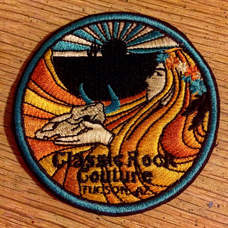 May include: A circular embroidered patch with a blue border and a yellow, orange, and white design. The patch features a stylized image of a woman with flowing hair and a sunburst in the background. The text "Classic Rock Soulvine Tucson, AZ" is embroidered in the lower portion of the patch.