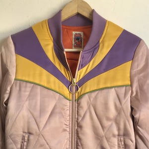 May include: A purple, yellow, and green striped bomber jacket with a quilted design. The jacket has a zipper closure and a small label with the text "Rock and Roll Cowgirl" on the front.