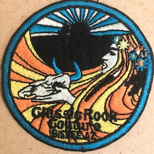 May include: A circular embroidered patch with a blue border. The center features a stylized image of a woman with long flowing hair, a sunrise, and the text "Grateful Rock Go Thru The Bister" in yellow and orange.
