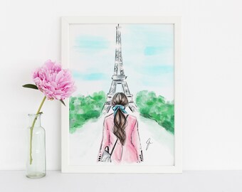 May include: Watercolour print of a person in a pink coat walking towards the Eiffel Tower in Paris. The artwork is framed in a white border. A pink peony in a glass vase is to the left of the framed print.