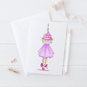 May include: A white card with a pink cupcake with a lit candle on top. The cupcake is being held by a girl wearing a sparkly purple dress and pink shoes.