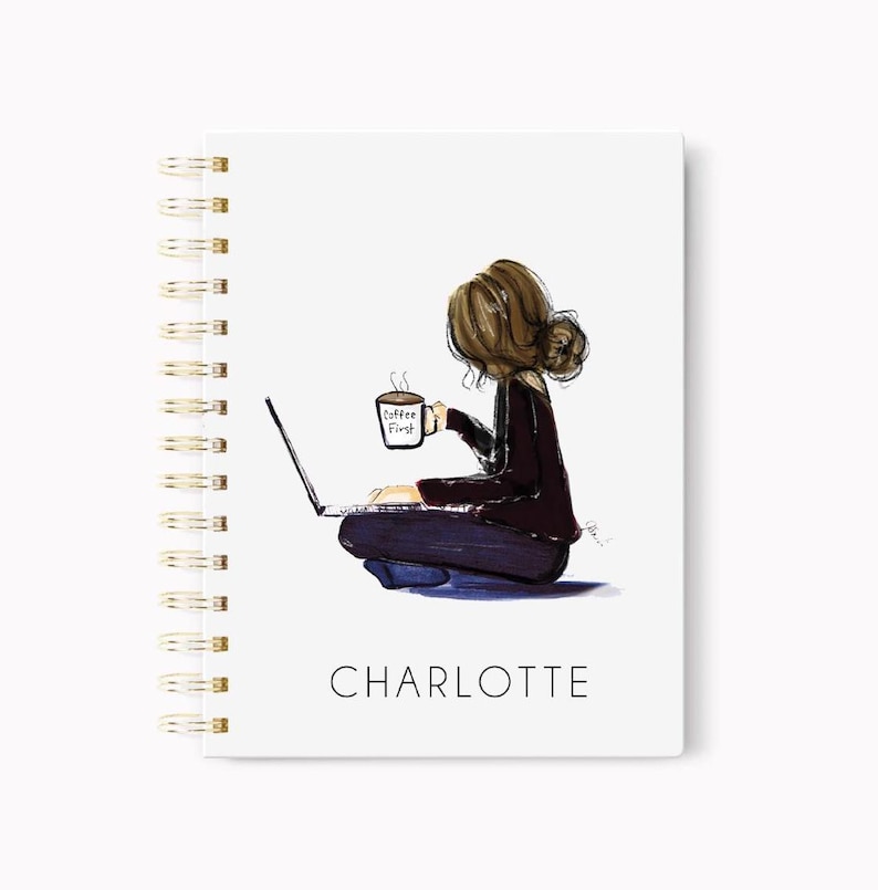 May include: A white spiral-bound notebook with a gold spine. The cover features an illustration of a person sitting with a laptop and a coffee mug that says "Coffee First." The name "CHARLOTTE" is printed below the illustration.