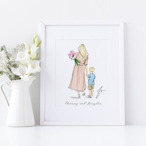 May include: A framed art print featuring a watercolor illustration of a woman and child. The woman wears a pink dress and holds flowers, walking with a young boy in a blue shirt and khaki shorts. The text "Mommy and Braylie" is below the image.