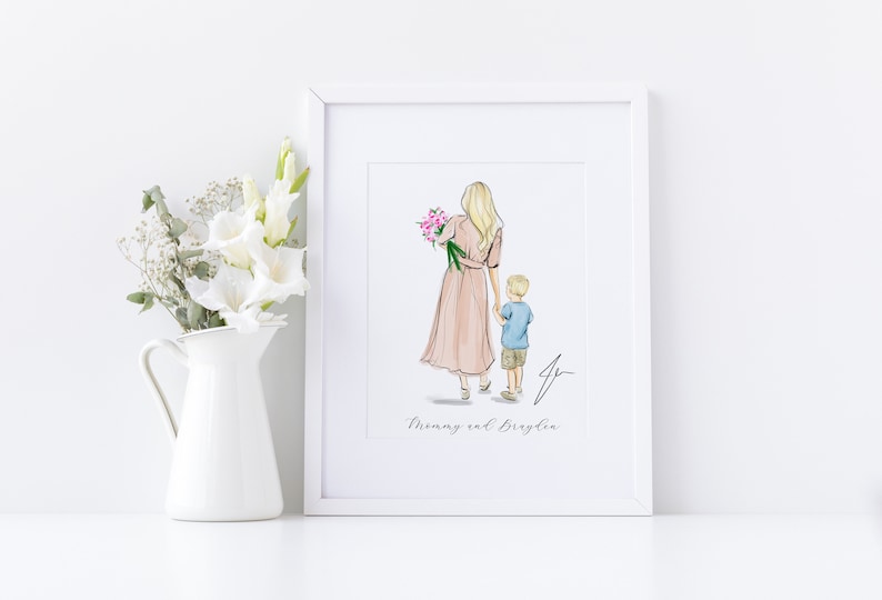 May include: A framed art print featuring a watercolor illustration of a woman and child. The woman wears a pink dress and holds flowers, walking with a young boy in a blue shirt and khaki shorts. The text "Mommy and Braylie" is below the image.