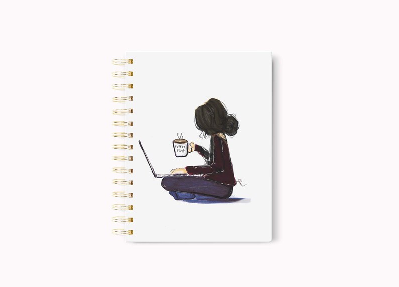 May include: A spiral-bound notebook with a whimsical illustration of a person sitting cross-legged, working on a laptop and holding a coffee mug. The mug reads "Coffee First". The notebook has a white cover and gold spiral binding.