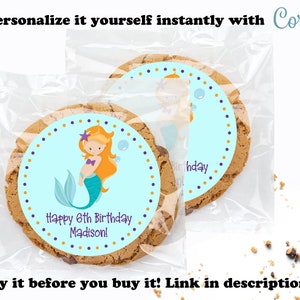 May include: A personalized cookie favor bag with a blue and purple mermaid sticker. The sticker says "Happy 6th Birthday Madison!" and has a mermaid with orange hair and a purple starfish on her head. The bag is clear plastic and has a brown cookie inside.