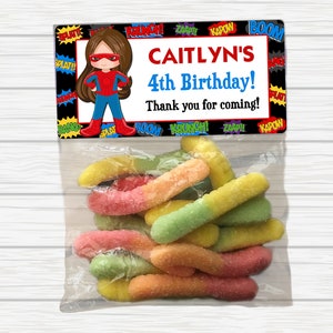 May include: A party favor bag with a colorful superhero-themed tag that says "CAITLYN'S 4th Birthday! Thank you for coming!" and a bag of colorful gummy worms.