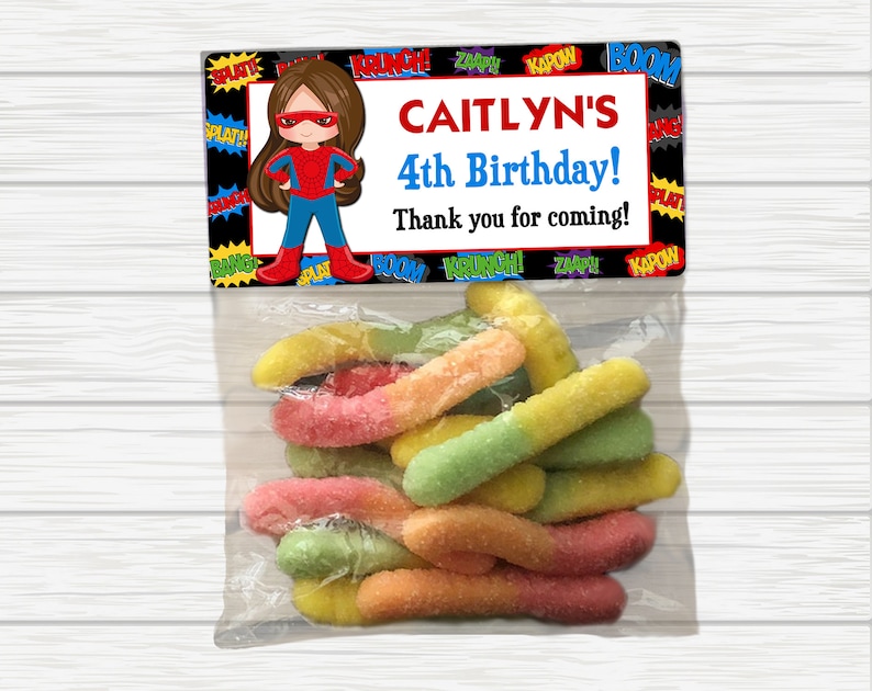 May include: A party favor bag with a colorful superhero-themed tag that says "CAITLYN'S 4th Birthday! Thank you for coming!" and a bag of colorful gummy worms.
