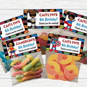 May include: Four favor bags with colorful candy and superhero themed labels. The labels have a black background with colorful text and images of girls dressed as superheroes. The text on the labels reads "CAITLYN'S 4th Birthday! Thank you for coming!" and "CAMERON'S 4th Birthday! Thank you for coming!"