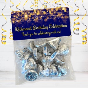 Puede incluir: Una bolsa de regalo azul y dorada con una etiqueta que dice "Richmond Birthday Celebration Thank you for celebrating with us!" La bolsa est&aacute; llena de besos de chocolate envueltos en papel plateado.