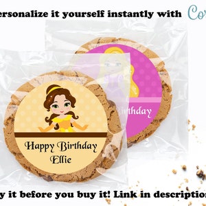 May include: A brown sugar cookie with a round sticker featuring a cartoon image of Belle from Disney's Beauty and the Beast. The sticker has a yellow background with a brown border and the text "Happy Birthday Ellie".