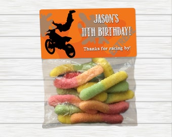 May include: A clear plastic bag filled with colorful gummy worms. A bright orange tag with a silhouette of a motocross rider and the text "Jason's 11th Birthday! Thanks for racing by!" is attached to the bag.