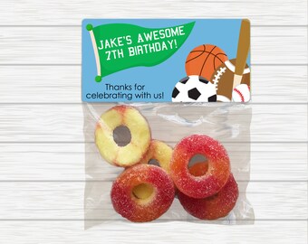 May include: A blue and green favor bag with a sports theme. The bag has a tag that says "Jake's Awesome 7th Birthday!" and "Thanks for celebrating with us!" The bag contains peach-flavored ring candies.