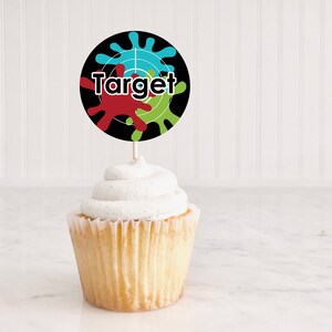 以下が含まれることがあります： 白いフロスティングをトッピングしたカップケーキ。黒と緑のターゲットをテーマにした丸いカップケーキトッパーには、白い文字で「Target」と書かれています。