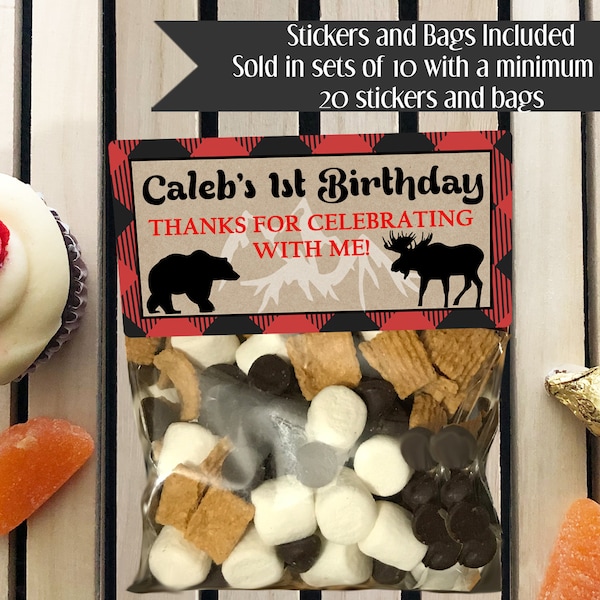 May include: A red and black plaid favor bag filled with chocolate chips, marshmallows, and graham crackers. The bag has a label that says "Caleb's 1st Birthday" and "Thanks for celebrating with me!" with a black bear and a moose illustration.