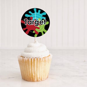 May include: A cupcake with white frosting topped with a round black and white paper cupcake topper with a target design and the word "Target" in white letters. The target design has red, green, and blue paint splatters.