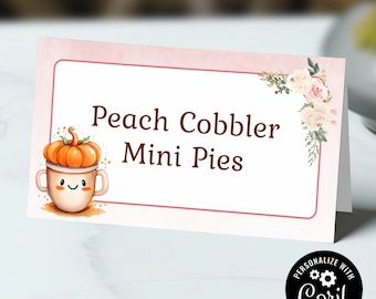 May include: Pink and white printable food label with a peach cobbler mini pies text and a cute cartoon pumpkin in a mug. The label has a floral design in the corner.
