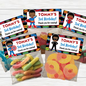 May include: Five small clear plastic bags filled with colorful candy. Each bag has a black and red superhero themed label with the text "TOMMY'S 3rd Birthday! Thank you for coming!"