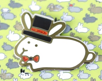 May include: White enamel pin of a rabbit wearing a black top hat with a red glitter band and a red bow tie. The pin is surrounded by a pattern of white and gray rabbits on a green background.