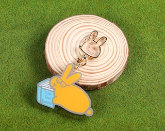 May include: A gold-colored keychain with a cartoon bunny reading a book that says "Train Your Hoomin". The bunny is yellow and the book is blue. The keychain also has a gold-colored ring.