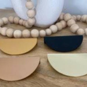 May include: Four half-circle shaped cabinet pulls in beige, cream, yellow, and black. The pulls have a stitched edge.