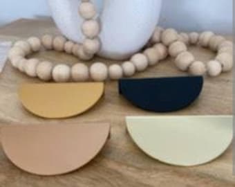 Könnte beinhalten: Vier halbkreisförmige Schrankgriffe in Beige, Creme, Gelb und Schwarz. Die Griffe haben einen genähten Rand.
