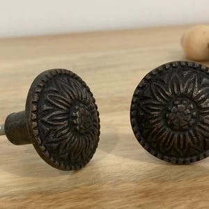 May include: Two antique bronze cabinet knobs with a floral design. The knobs are round and have a screw on the back.