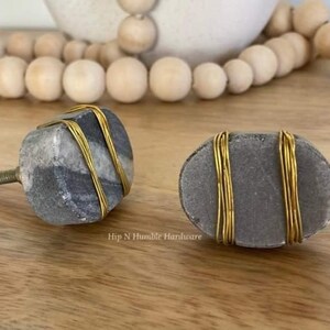 May include: Two grey marble cabinet knobs with gold wire accents. The knobs are oval shaped and have a textured surface.