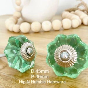 May include: Two green glass cabinet knobs with a silver metal base. The knobs are shaped like a flower with six petals. The text on the image reads "D 45mm P 30mm Hip N Humble Hardware".