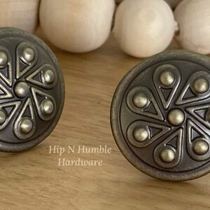 May include: Two antique brass cabinet knobs with a decorative floral design. The knobs are circular in shape with a raised centre and a textured finish.