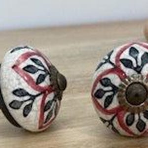 May include: Two white ceramic cabinet knobs with a red and black floral design. The knobs have a brass screw.