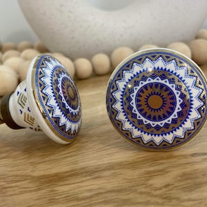 May include: Two white ceramic cabinet knobs with a blue and gold mandala design. The knobs are round and have a raised design.