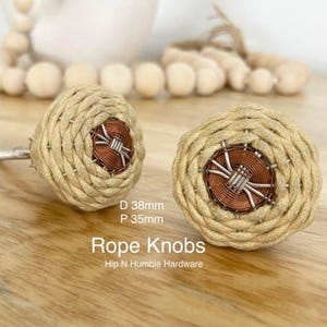 May include: Two beige rope knobs with a copper and silver centre. The knobs are 38mm in diameter and 35mm in projection. The text "Rope Knobs" and "Hip N Humble Hardware" is below the knobs.