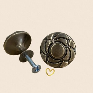 May include: Two antique bronze cabinet knobs. One knob is a rounded shape with a decorative floral design. The other knob is a mushroom shape. Both knobs have a bronze finish and include the necessary hardware for installation.