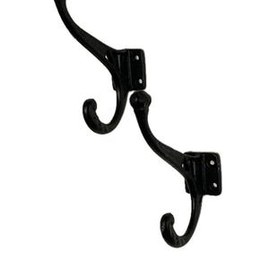May include: Two black cast iron hooks with a decorative scroll design. Each hook has two prongs and a rectangular base.