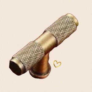 May include: A gold-toned T-shaped cabinet knob with a textured surface.