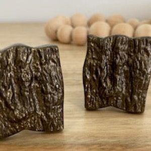 May include: Two square-shaped cabinet knobs with a wood grain texture and a bronze finish.