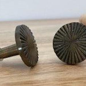 May include: Two antique brass cabinet knobs with a sunburst design. The knobs have a slightly textured finish and are round.