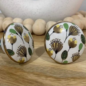 May include: Two white ceramic cabinet knobs with a gold trim. The knobs feature a floral design with yellow, green, and brown accents.