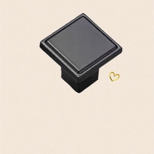 May include: Black square cabinet knob with a slightly raised edge.