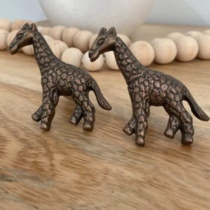May include: Two bronze giraffe drawer pulls with a textured finish. The giraffes are facing different directions and have a detailed design.