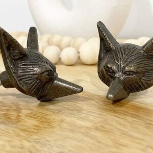 May include: Two metal fox head drawer pulls with a distressed finish. One pull has a screw attached to the back.